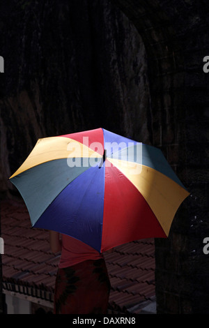 WOMAN & MULTI-COLOURED UMBRELLA ALUVIHARA ROCK CAVE TEMPLE MATALE SRI LANKA 11 March 2013 Stock Photo