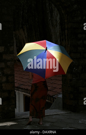 WOMAN & MULTI-COLOURED UMBRELLA ALUVIHARA ROCK CAVE TEMPLE MATALE SRI LANKA 11 March 2013 Stock Photo