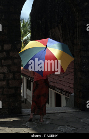 WOMAN & MULTI-COLOURED UMBRELLA ALUVIHARA ROCK CAVE TEMPLE MATALE SRI LANKA 11 March 2013 Stock Photo