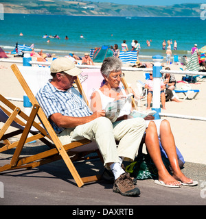 Couple sitting in deck chairs reading at Weymouth beach, Dorset, UK. Stock Photo