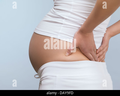 Pregnant woman rubbing her back, closeup of midsection Stock Photo