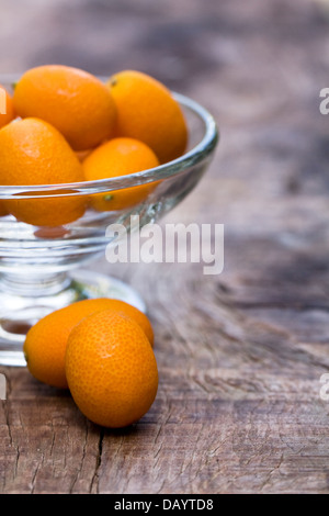 Kumquats in a glass bowl on a wooden board. Stock Photo