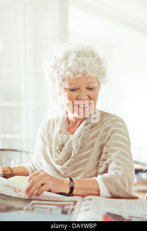 Old lady at home smiling while reading the news Stock Photo