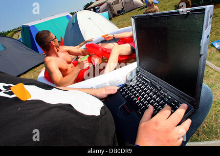 A participant of the 'Chaos Communication Camp 2007' works on his laptop in the sun next to others bathing in an inflatable pool on the compounds of the Aviation Museum ('Luftfahrtmuseum') Finowfurt, Germany, 9 August 2007. Around 1,200 computer enthusiasts from Germany and elsewhere have gathered for the five day summer camp, which sees itself as 'open air festival for hackers and Stock Photo