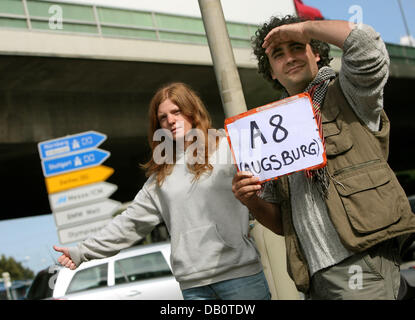 Marie Clermontelle lifts her thumb and her boy-friend holds a sign indicating their destination while they are waiting for a lift in Munich, Germany, 23 August 2007. Photo: Tobias Hase Stock Photo