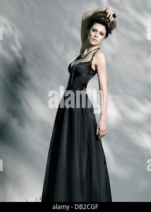 License available at MaximImages.com Beautiful woman in long black vintage dress on gray background in tree shadow Stock Photo