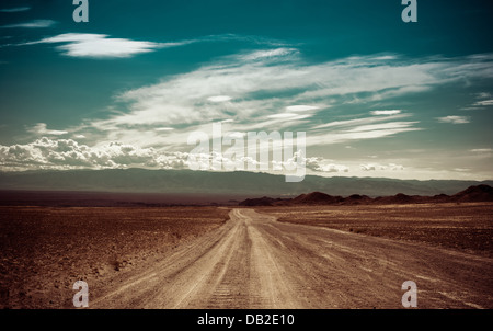Empty rural road going through prairie under cloudy sky in Charyn canyon. State National Paleontology Park in Kazakhstan Stock Photo