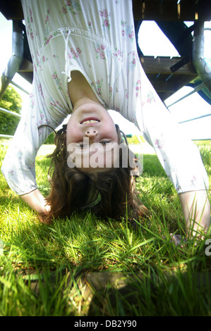 small female child hanging upside down whilst playing in her own garden Stock Photo