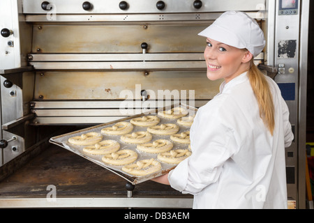 Baker in bakery holding baking tray with pretzels at the oven Stock Photo