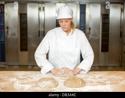Baker kneading bread dough in bakery on a table at the oven Stock Photo