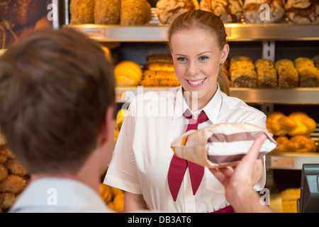 Saleswoman or shopkeeper in bakery handing over a bag full of bread to customer Stock Photo