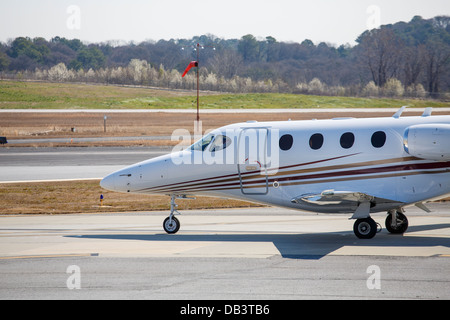 A private jet taxiing onto a runway of a small regional airport by a windsock Stock Photo