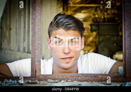 Attractive young man at rusty window with funny expression on his face, looking in camera Stock Photo