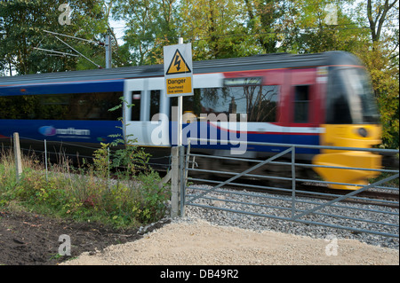 Local passenger train engine running on Wharfedale line, speeds & travels past gate & safety warning sign - Esholt, West Yorkshire, England, UK. Stock Photo