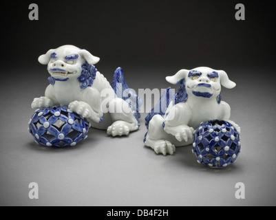 This pair of okimono figures, featuring Chinese lions on pierced balls, are crafted from ivory and exhibit detailed carving. They symbolize protection and are a fine example of Japanese craftsmanship in sculpture. Stock Photo