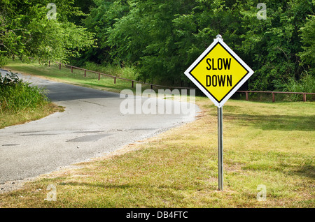 Slow Down yellow traffic sign on the roadside against green woods Stock Photo