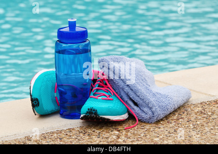 Blue water bottle with running shoes and towel by pool. Exercise and hydration concept. Stock Photo