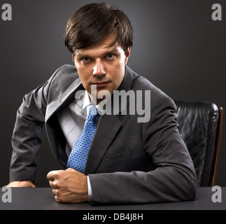 businessman sitting behind his desk looking at the camera on gray Stock Photo
