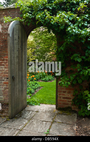 An open wooden garden door provides a 'Secret Garden' view of the Philosopher's Garden at Cottesbrooke Hall, Northamptonshire, England