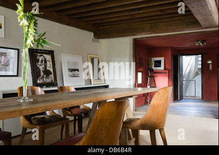 Table and chairs with beamed ceiling and artwork in Antwerp apartment of Boris Vervoordt Stock Photo