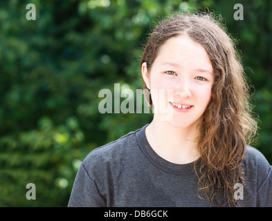 Photo of young girl smiling while looking forward with blurred out bright green trees in background Stock Photo