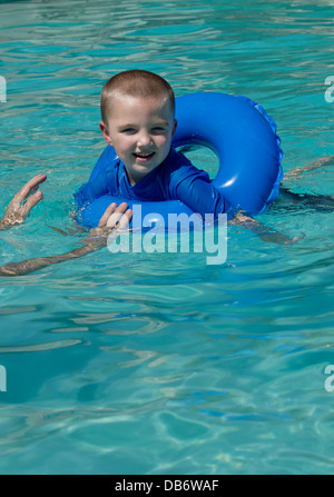 A six year old boy with autism smiles while playing with his dad in the pool. Stock Photo