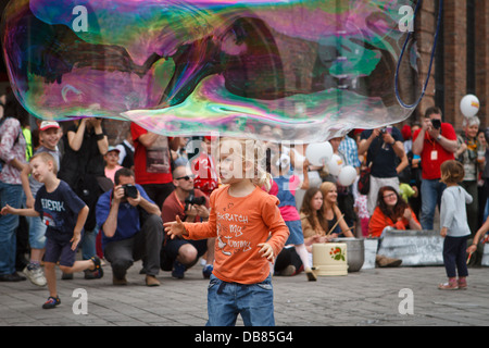 A girl catching big soap bubble during 'Industriada' 2013 street performance at Nikiszowiec main square. Katowice, Poland. Stock Photo