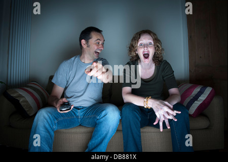 couple watching television together pointing laughing and being shocked Stock Photo