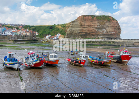 A line of fishing boats lie on the sand at low tide in Staithes Harbour North Yorkshire in front of Cowbar Nab cliff Stock Photo