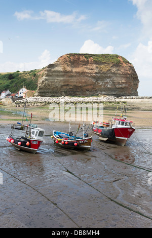 A line of fishing boats lie on the sand at low tide in Staithes Harbour North Yorkshire in front of Cowbar Nab cliff Stock Photo