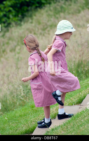 two young children 5 to 6 years old in red school uniform playing on steps in park close up one with hat. Stock Photo