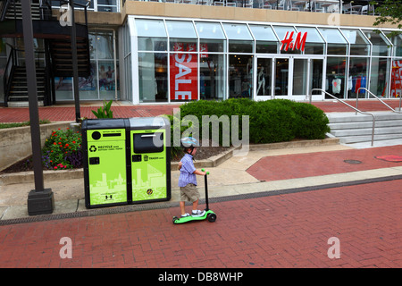 Boy riding scooter past BigBelly solar powered, rubbish-compacting and recycling bins, Inner Harbor, Baltimore , Maryland, USA Stock Photo