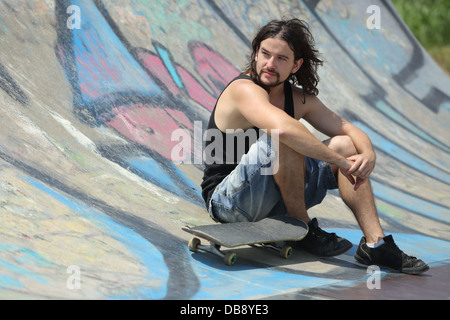 Portrait of a boy sitting with a skateboard on a half pipe with graffiti Stock Photo