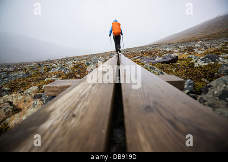 Female hiker walks along wooden planks in Tjäktjavagge on Kungsleden trail, Lappland, Sweden Stock Photo