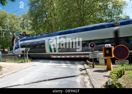 A high speed SNCF TGV train speeding, motion blurred through a railway crossing with the barriers down and red light lit, France Stock Photo