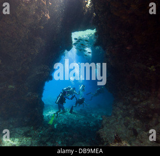 Scuba divers exploring an underwater sea cave in a tropical coral reef Stock Photo