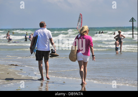 Couple on hot day at West Wittering Blue Flag beach, nr. Chichester, West Sussex, UK watch holidaymakers enjoy swimming. Stock Photo