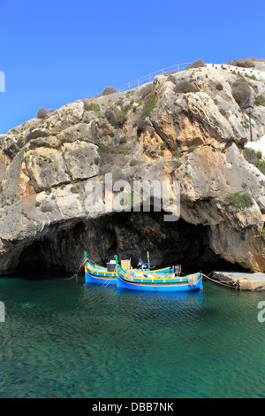 Luzzu traditional fishing boats moored at the mouth of Caroline Cave on the right cliffs of Xlendi Bay situated in the south west of Gozo the sister island of Malta Stock Photo