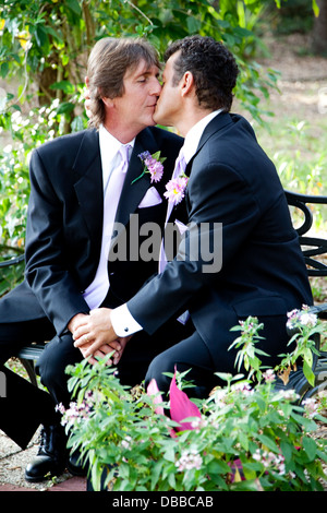 Handsome gay wedding couple kissing outdoors in the garden on their wedding day.  Stock Photo