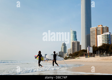 Surfers walking into surf with city skyline in background. Surfers Paradise, Gold Coast, Queensland, Australia Stock Photo