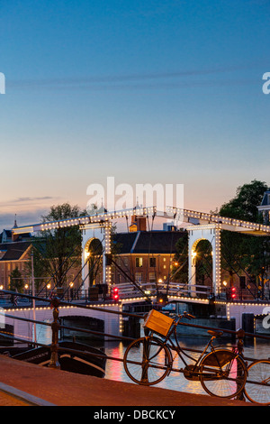 Amsterdam Magere Brug, Skinny Bridge, on the Amstel River and Hermitage Museum at dusk night evening in summer Parked bicycle Stock Photo