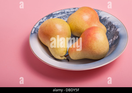 Fresh ripe Bartlett Pears in a blue china bowl on a pink background. Stock Photo