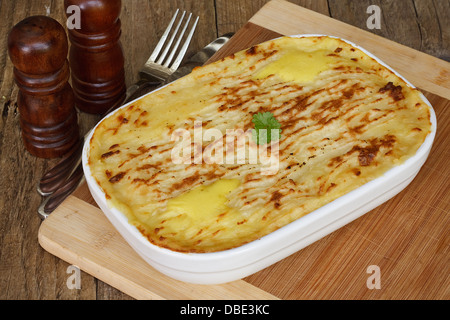 Traditional Homemade Fish Pie in a casserole dish with crispy mashed potato on a rustic kitchen table setting Stock Photo