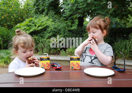 Twin girls having a snack in the park.