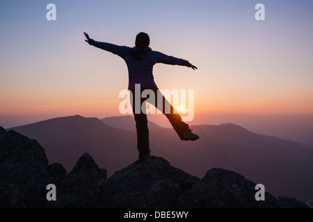 Silhouette as female hiker balances on rock viewing mountain sunset from summit of Glyder Fach, Snowdonia national park, Wales Stock Photo