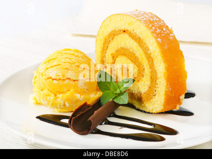Slice of Swiss roll with yellow ice cream and chocolate sauce Stock Photo