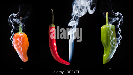 Smoke comes out of tips of hot chilli peppers in orange red and green Stock Photo