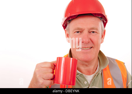 Smiling construction working wearing red safety helmet and holding a red mug of builder's tea. Stock Photo