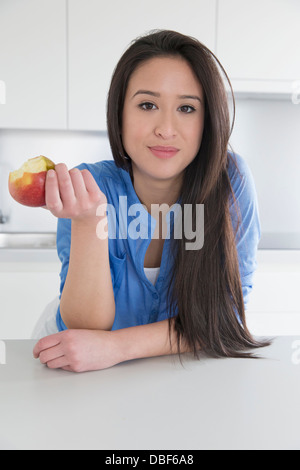 Mixed race woman eating fruit in kitchen Stock Photo