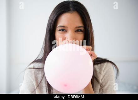 Mixed race woman blowing up balloon Stock Photo